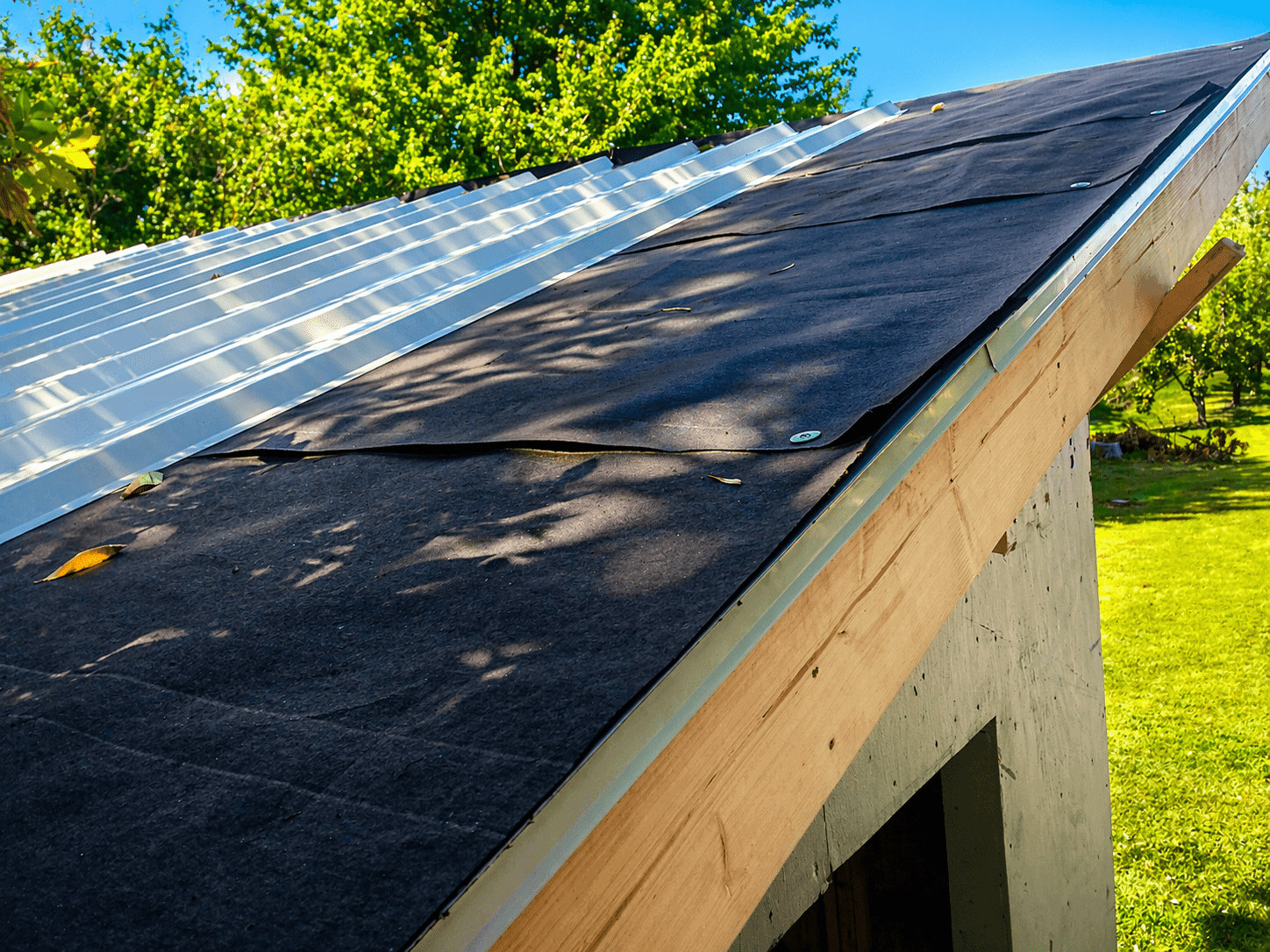 Roof with felt rolled out and metal roofing panels being installed