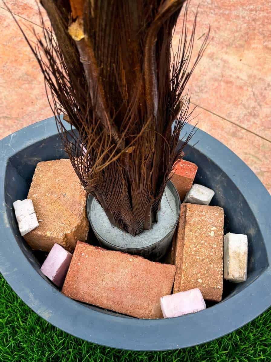 Styrofoam wedges packed between bricks at the base of an artificial palm to prevent wobble in wind