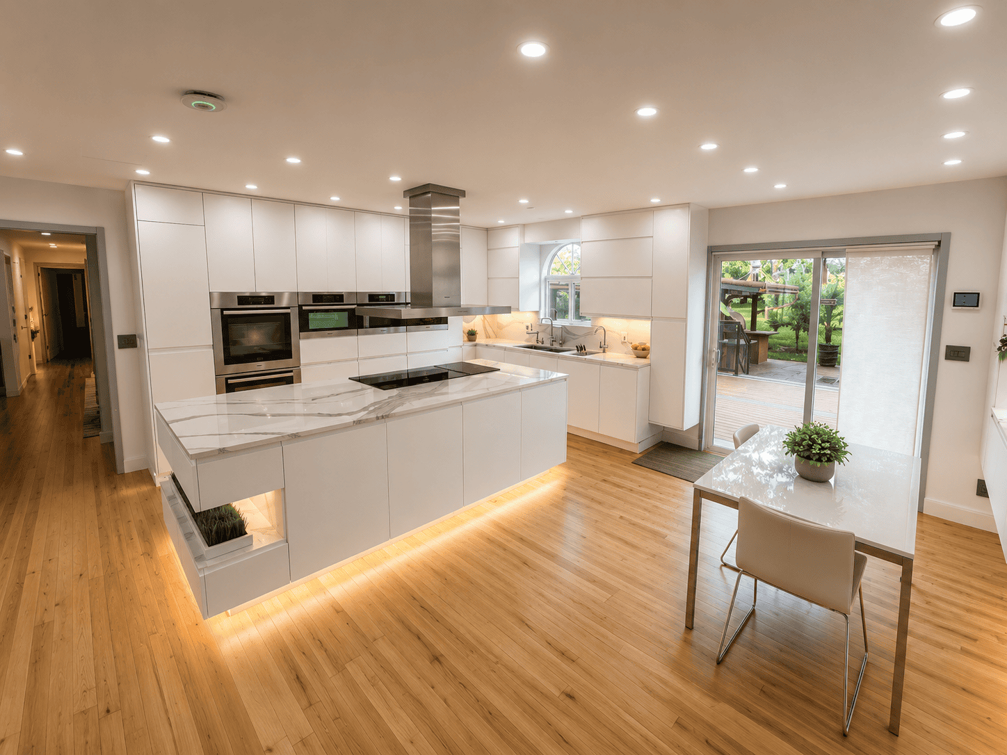 Modern kitchen with white cabinetry, marble countertops, and stainless steel appliances, featuring a dining table with a potted plant and large sliding door opening to an outdoor area.