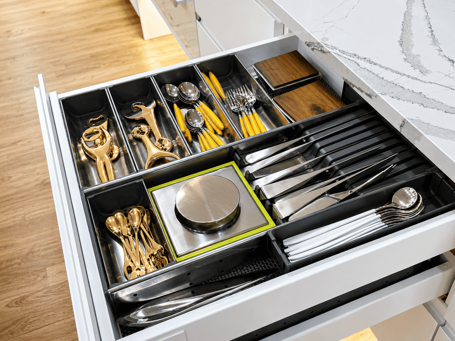 A neatly organized kitchen drawer containing various utensils, including gold-colored cutlery, measuring tools, and storage containers.