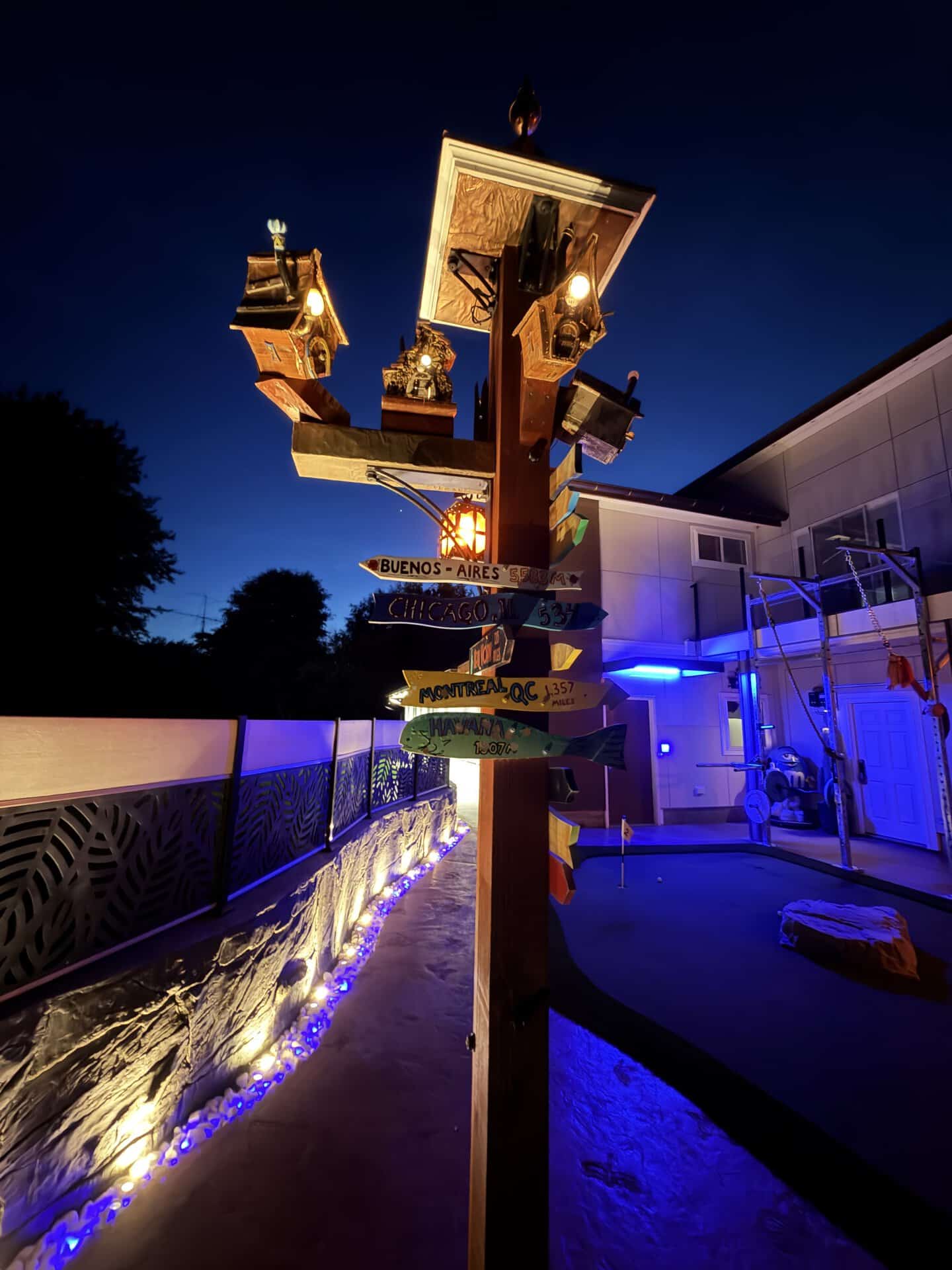 DIY lamppost village lit at night with LED-glowing birdhouse windows and illuminated directional signs