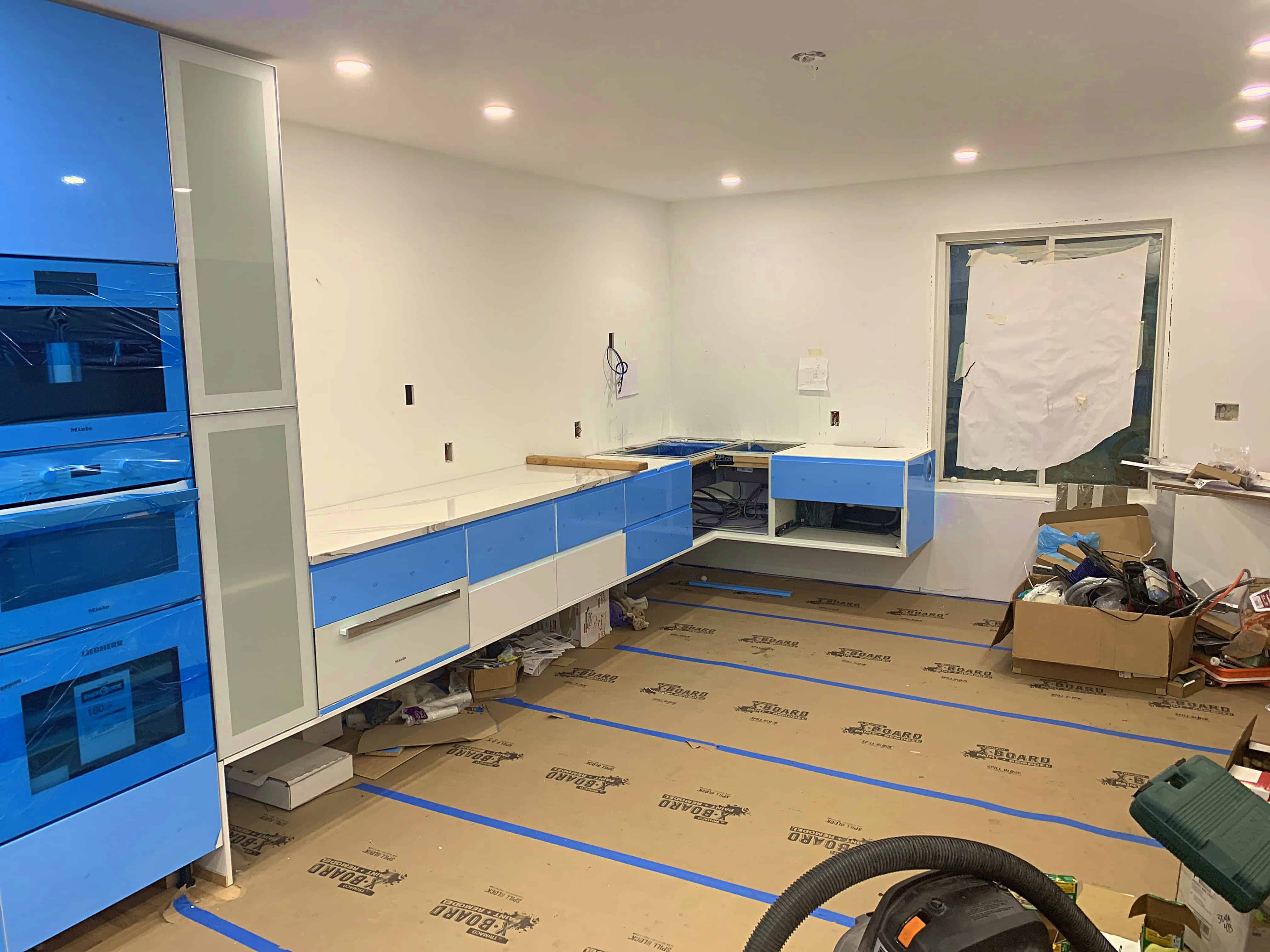 A modern kitchen under construction, featuring blue cabinets, a white countertop, and various tools and materials on the floor.