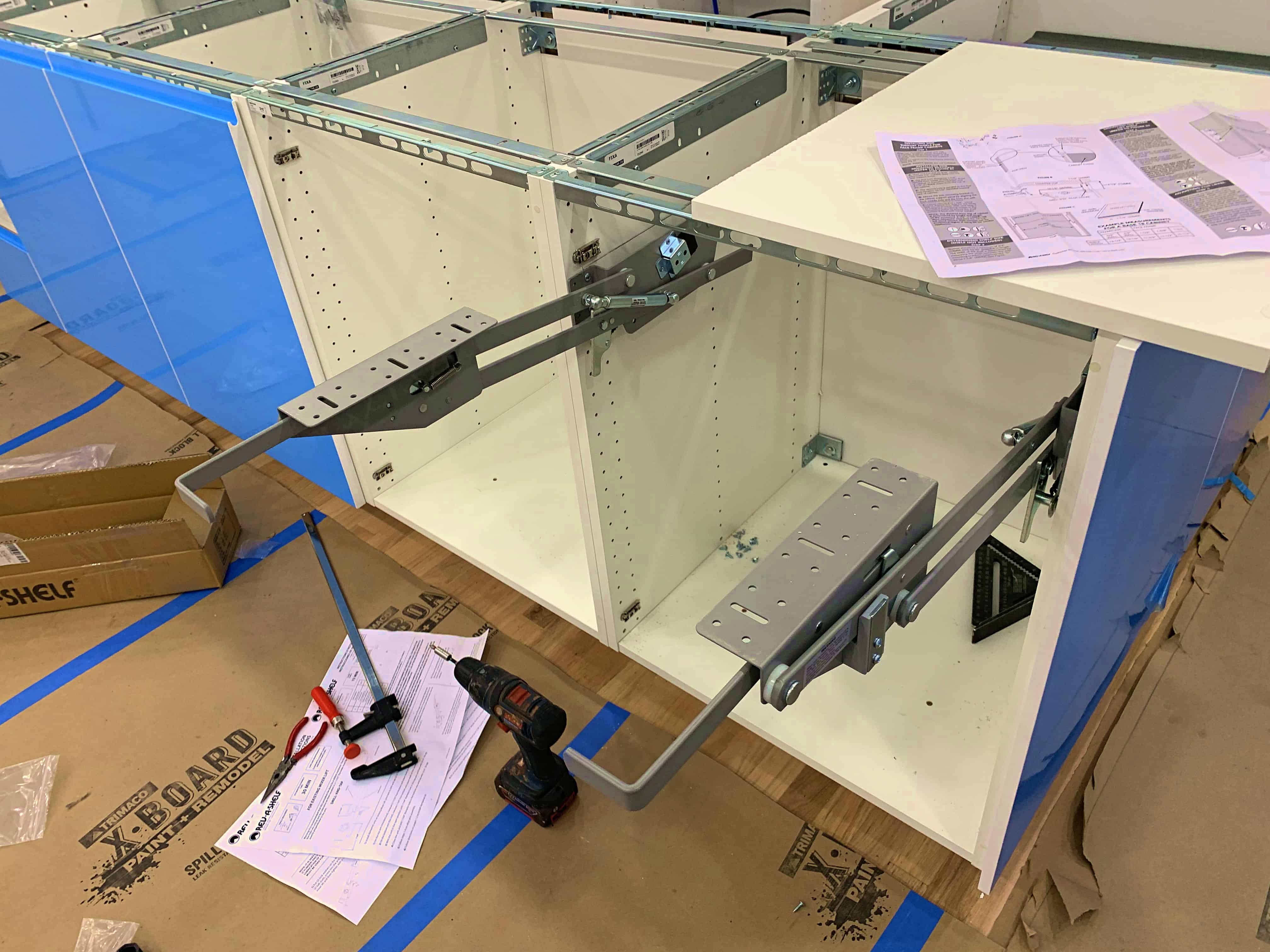 An image showing the assembly of a cabinet with rails and brackets, accompanied by tools like a drill and clamps, and instruction manuals on a flat surface.