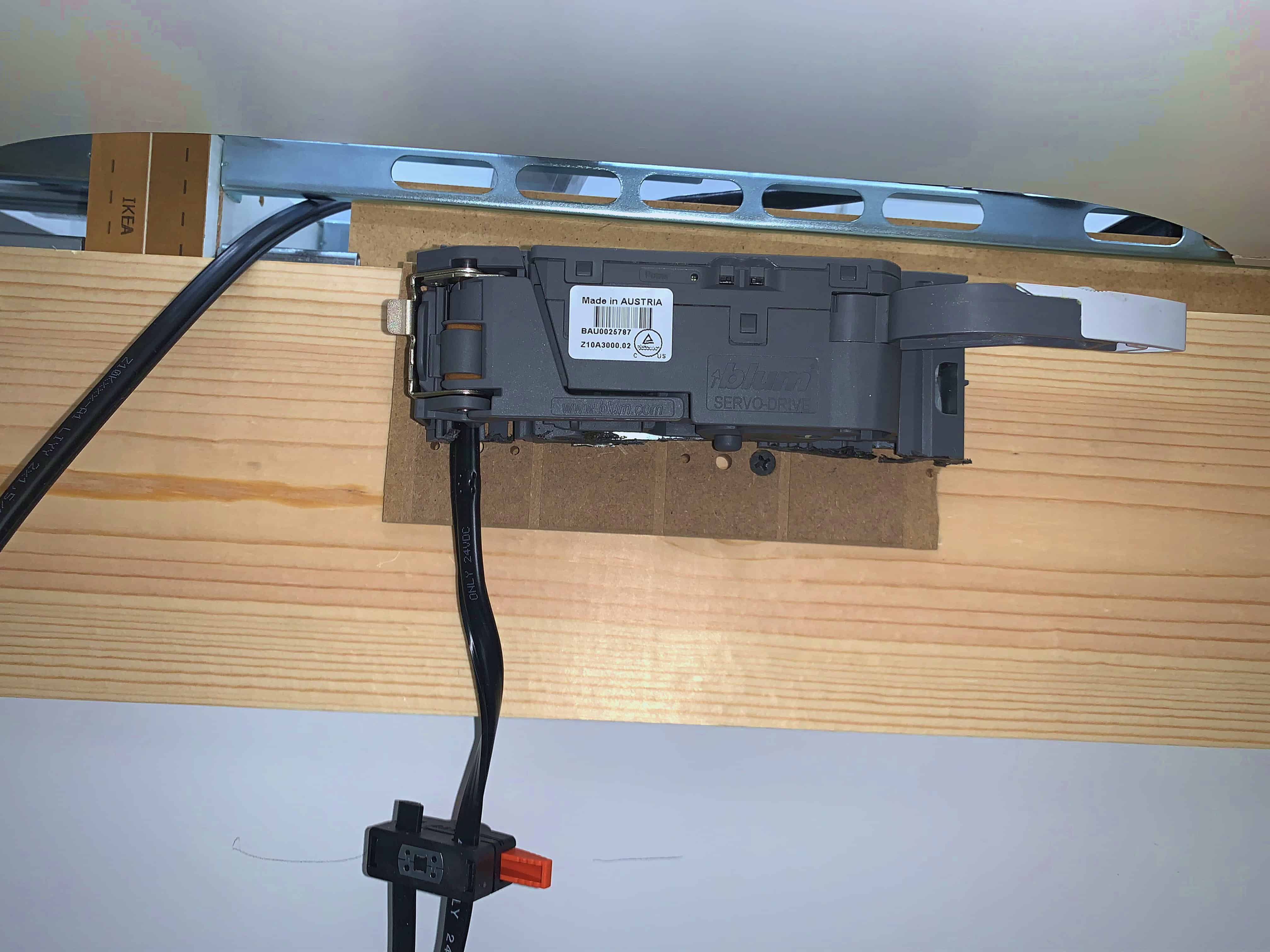An electrical component mounted on a wooden surface, featuring wiring and labels, possibly related to a servo-drive mechanism.