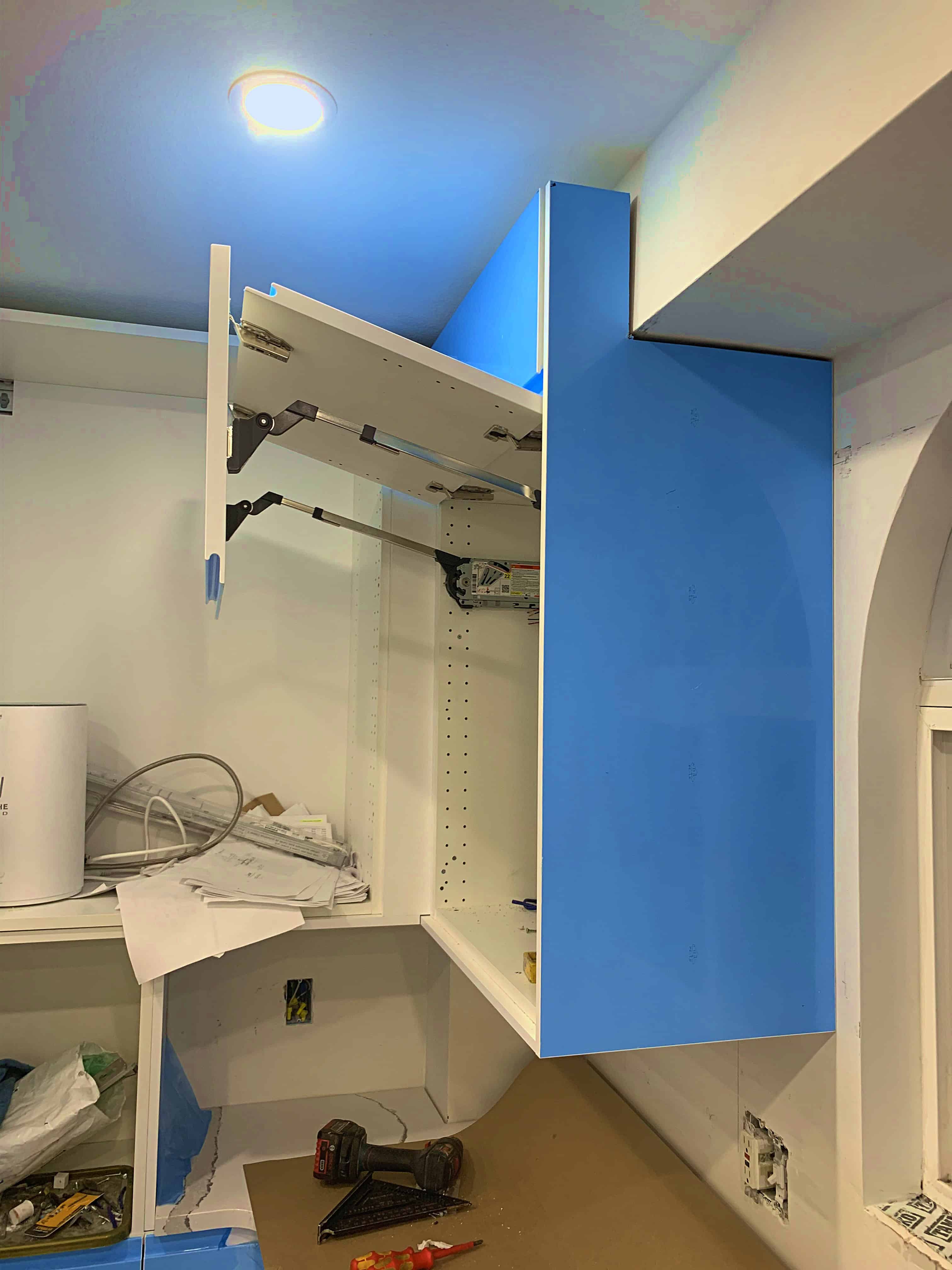 Partially opened kitchen cabinet with a blue door, showing internal components and installation tools.
