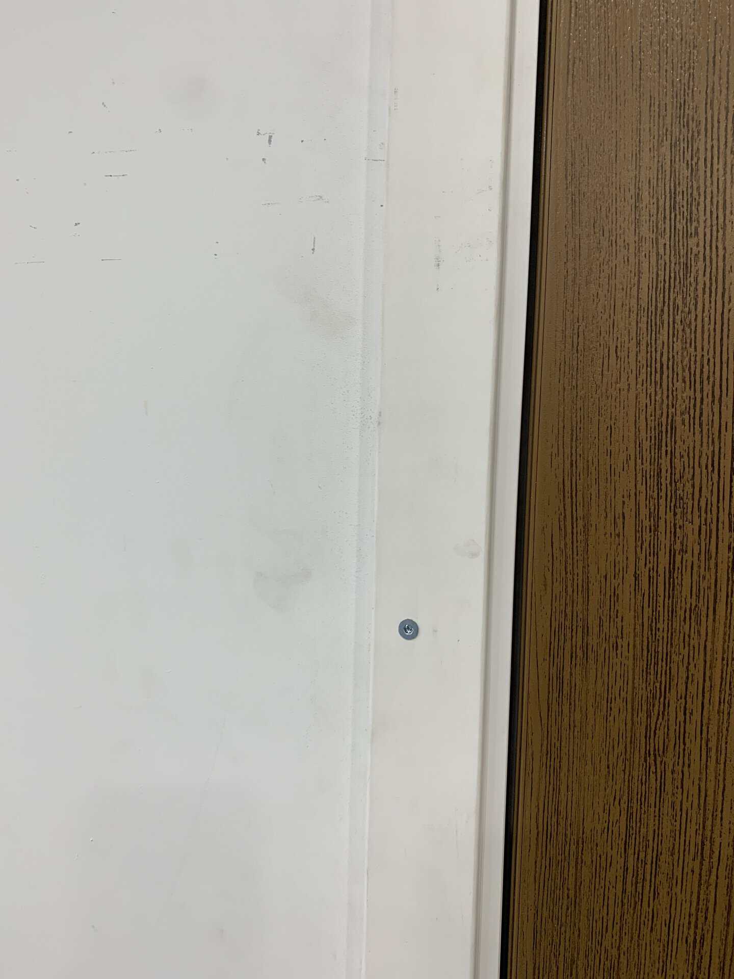 Close-up of a white wall and wooden door frame with a screw.