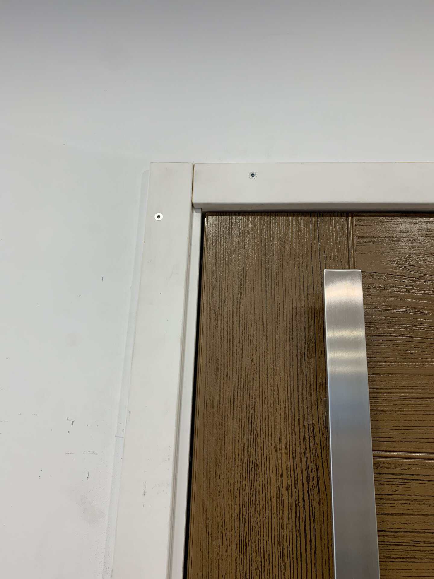 Close-up of a modern wooden door with a metallic handle and white wall frame.