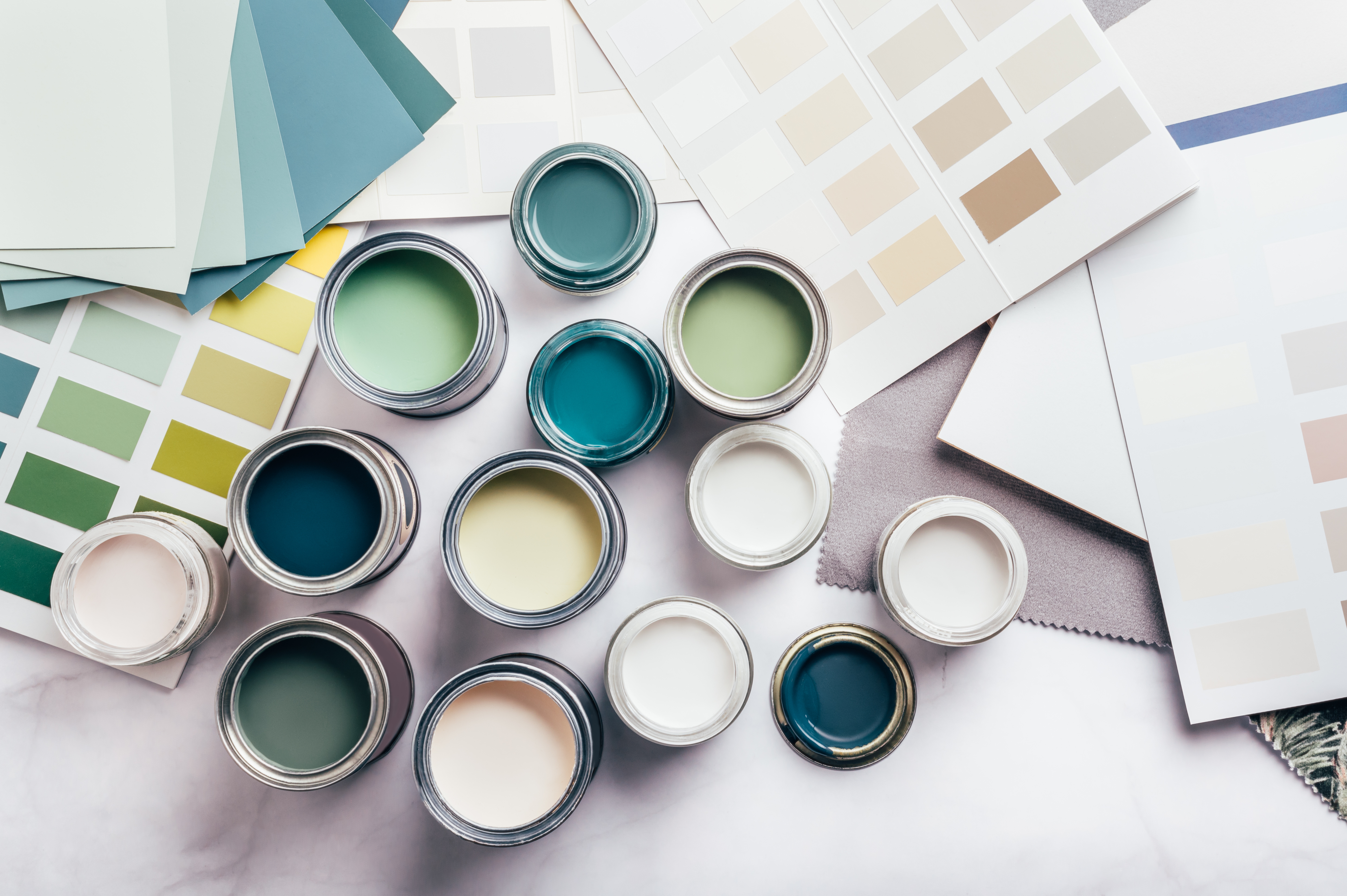Tiny sample paint cans during house renovation, process of choosing paint for the walls, different green and beige colors, color charts on background