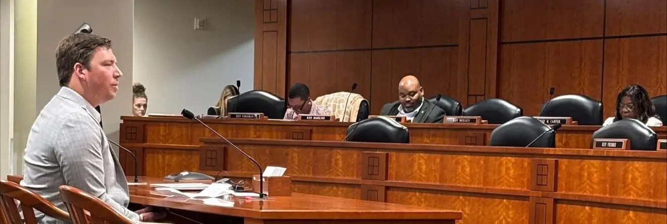 A man sitting in a court room testifying in front of a judge.
