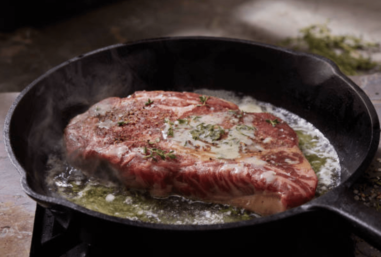 Steak cooking in butter and oil with herbs in cast iron skillet