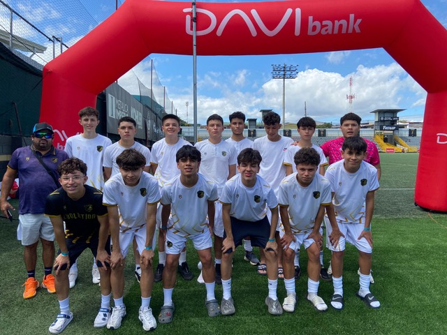 Equipo de jóvenes futbolistas posando frente a un arco inflable de la marca Davi Bank, en un campo de fútbol.