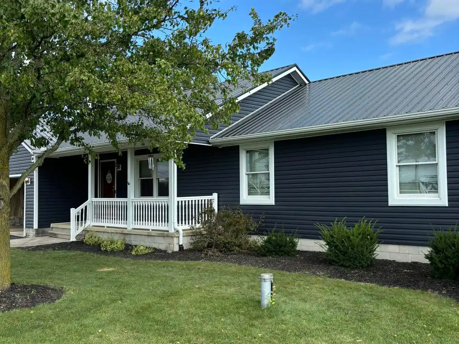 Modern navy blue siding home with white trim, featuring new windows and a small front porch, surrounded by well-maintained lawn and landscaping, showcasing home improvement services.