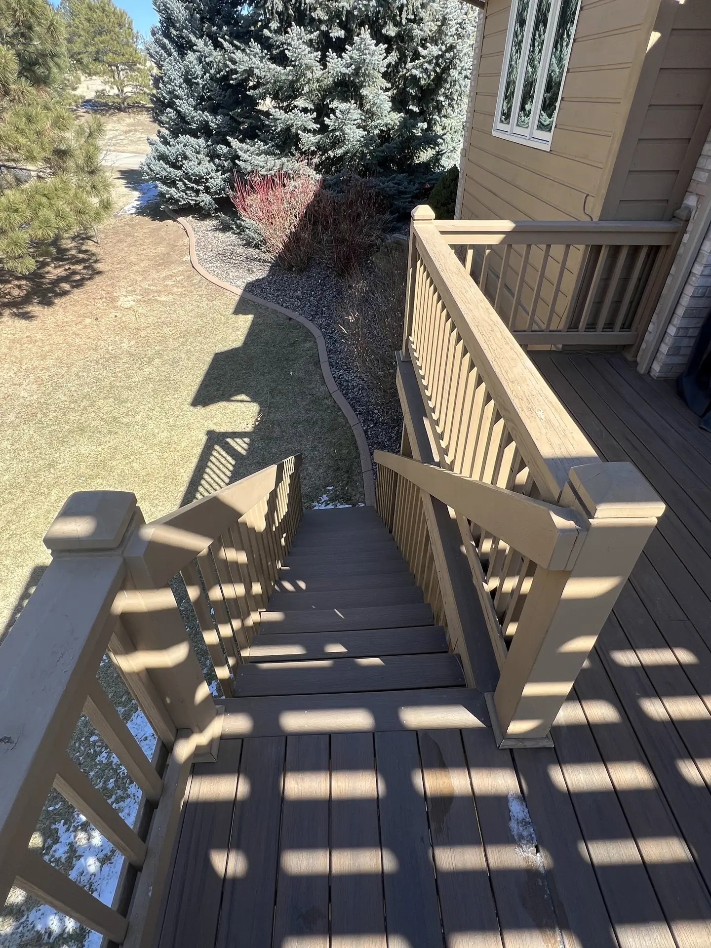 View looking down composite deck stairs with wood railing into the yard