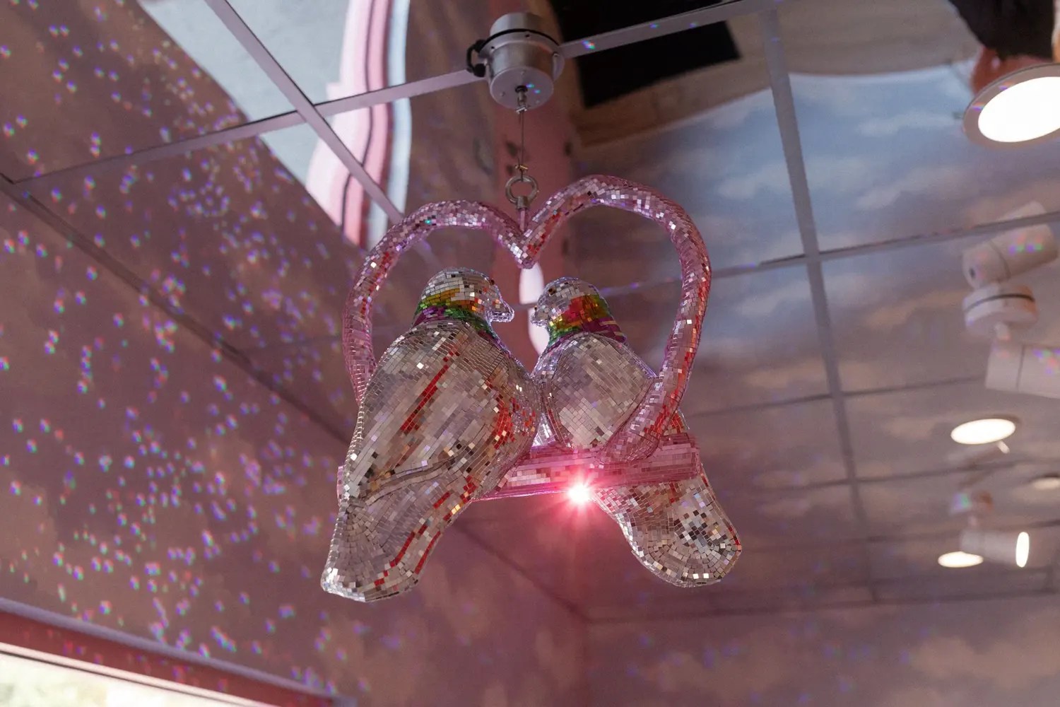 Boule disco de pigeon en miroir personnalisée de deux pigeons à l'intérieur d'un cœur rose pailleté suspendu au plafond peint en nuage à Sure Thing Chapel NYC