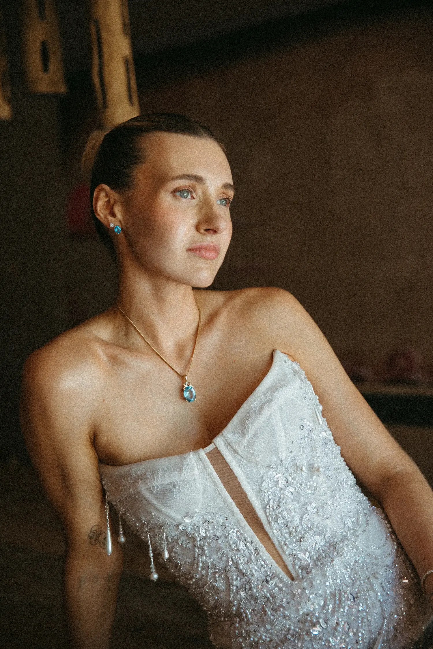 Close-up of the bride wearing a vivid aqua topaz pendant necklace and matching earrings with her beaded corset gown.