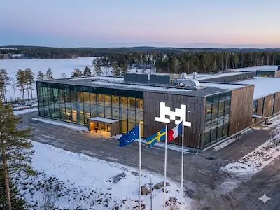 Modernes Rechenzentrum im Schnee mit Glasfassade und Fahnen vor Wald und See.