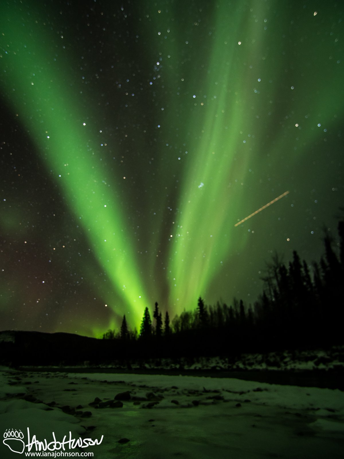 A plane streaks through the aurora over the Chena River.