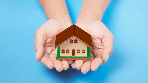 Image of two hands holding a small home, symbolizing home care. The background is blue, representing calmness and serenity. The image portrays the care and support provided to seniors in their own homes through home care services.