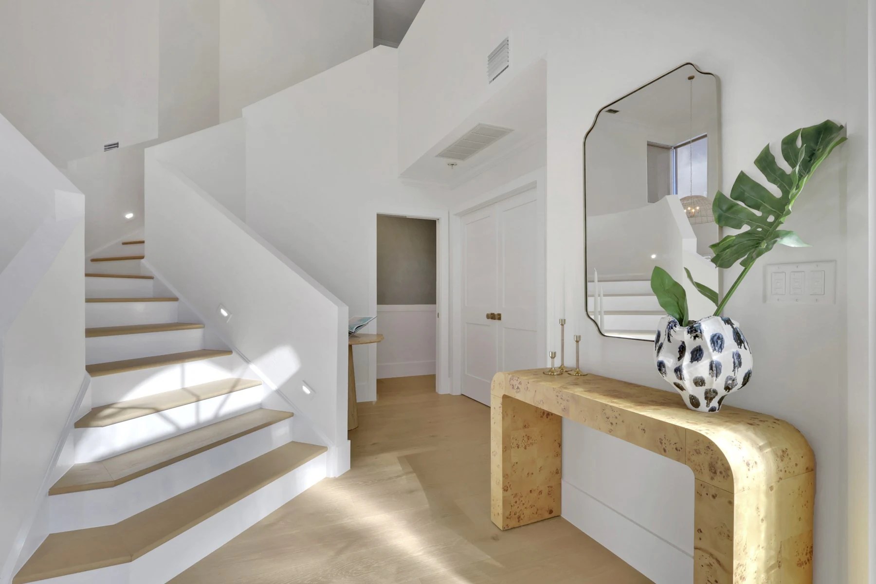 Entry with a burl console, a sculptural mirror and a white staircase, designed by Iglesias Design Group