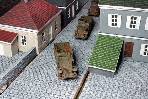 Flames of War British M5 Half Tracks trundle down the cobbled street in Normandy.