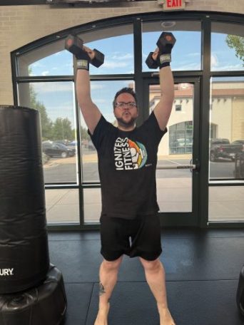 Ignited Fitness member standing besidea heavy bag lifting dumbbells