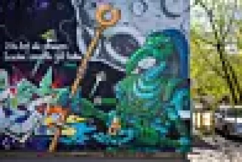 technology Colorful graffiti mural beside a tree-lined street with parked cars in Warsaw, Poland.