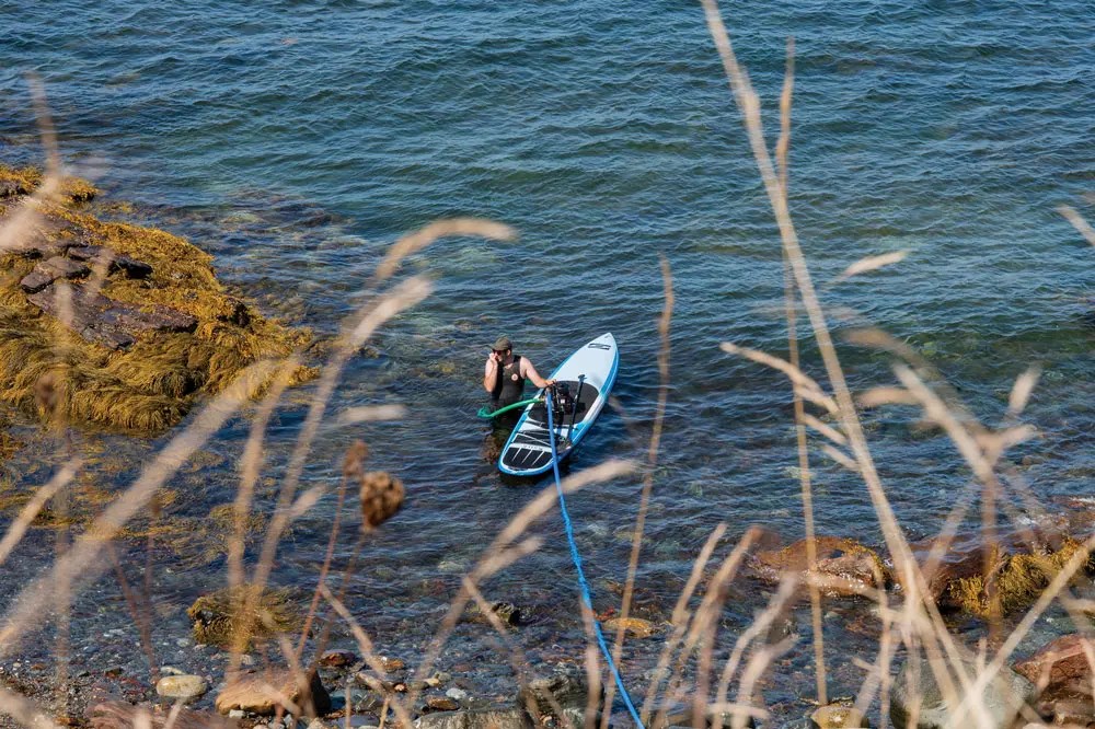 Pelletier placing a small pump and a 400-foot-long hose in the ocean to pump seawater to the tables in the greenhouse
