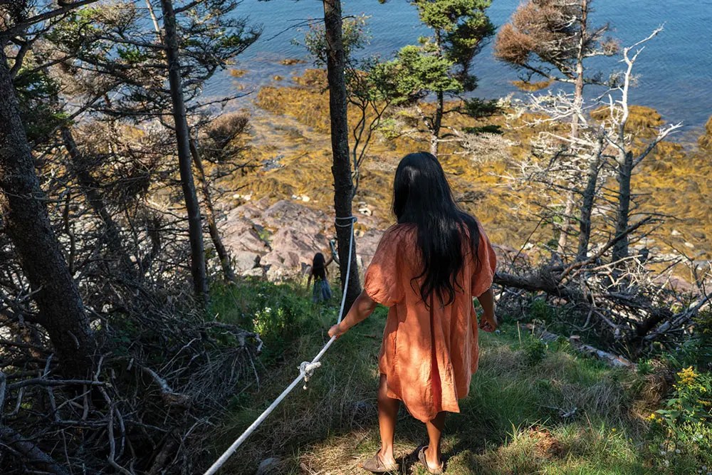 Usha Beaudoin holding onto a rope looking out over the cliff edge 