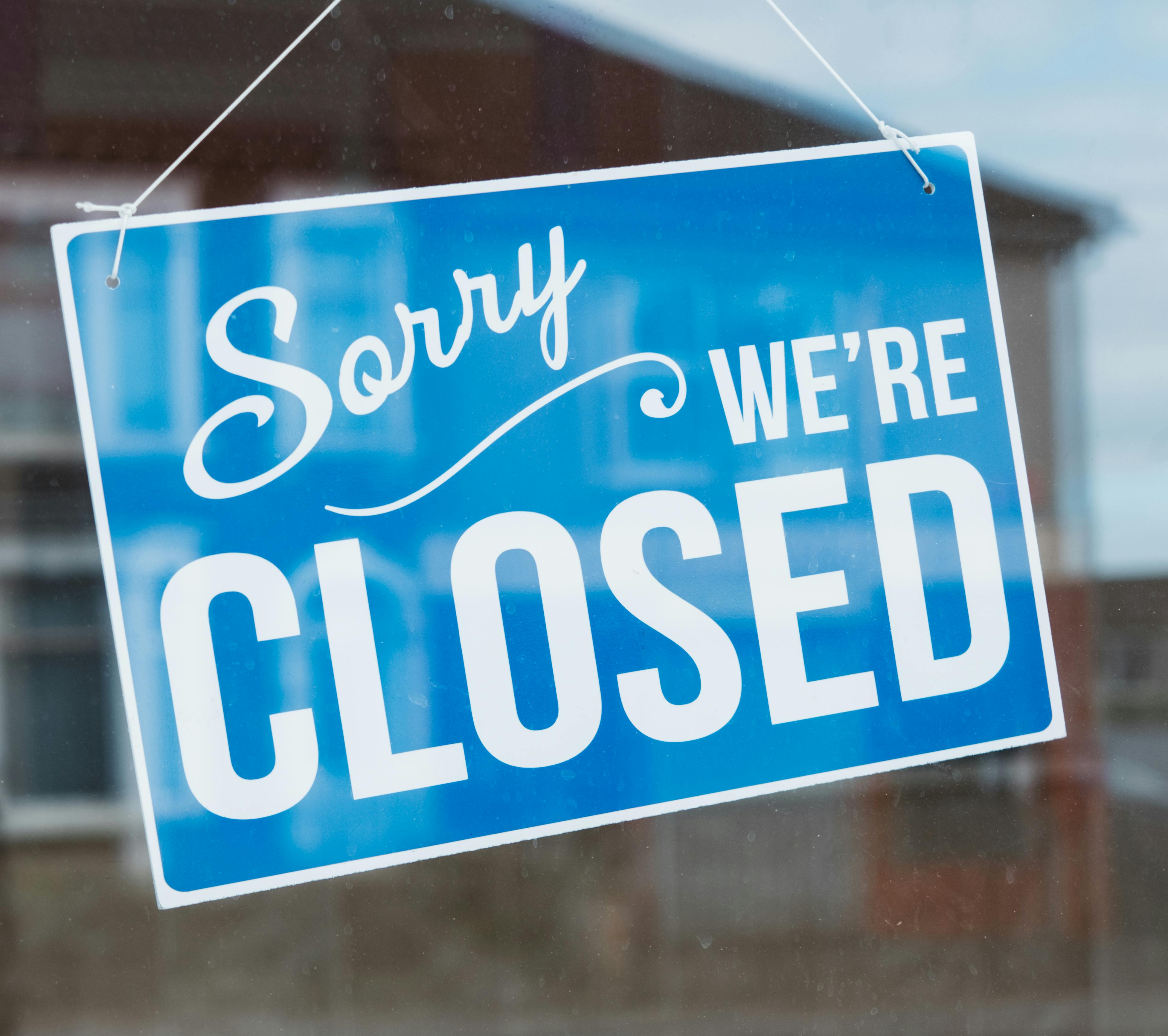 A blue and white 'Sorry We're Closed' sign hanging on a glass door.