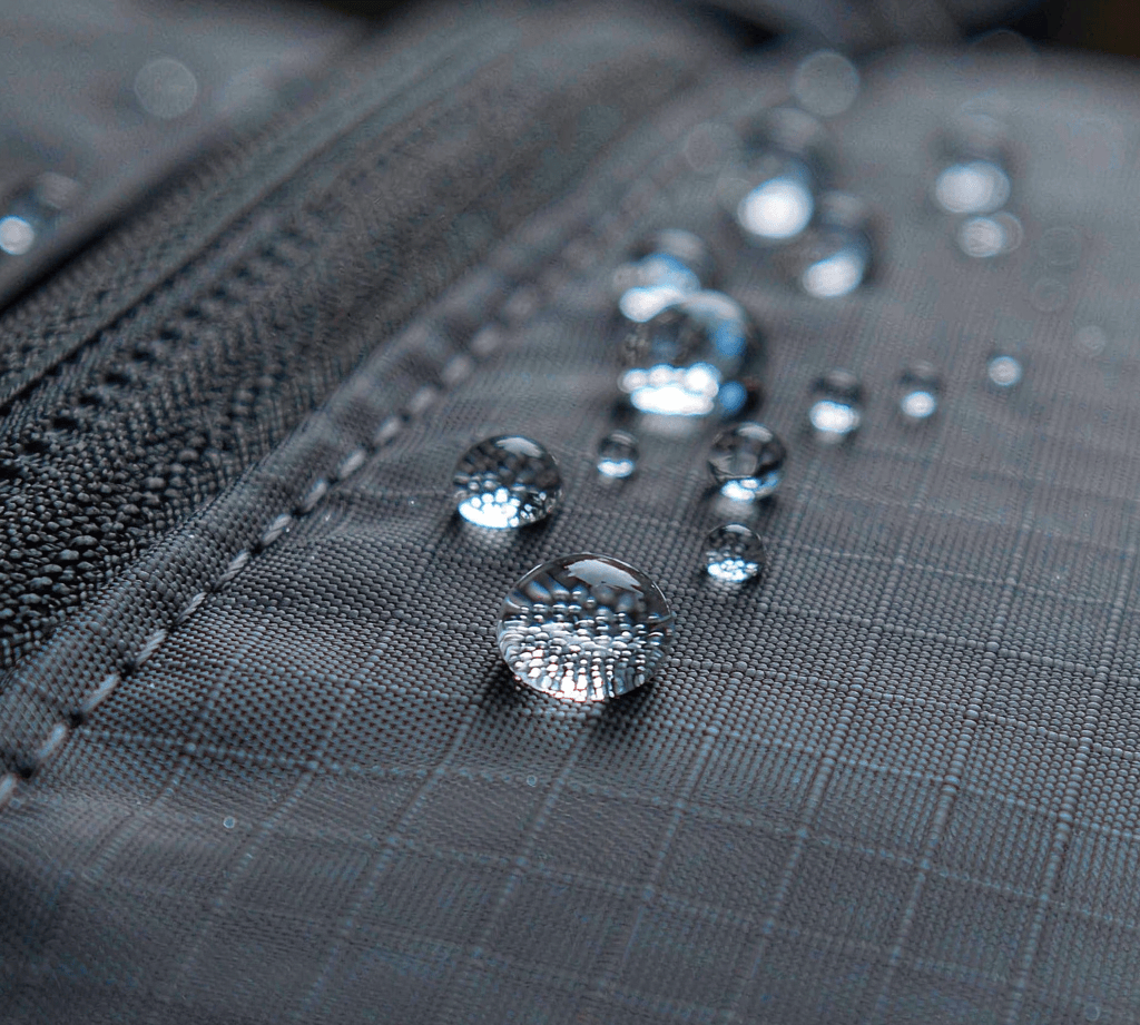 Close-up of water droplets beading on dark ripstop nylon fabric with a durable water repellent finish