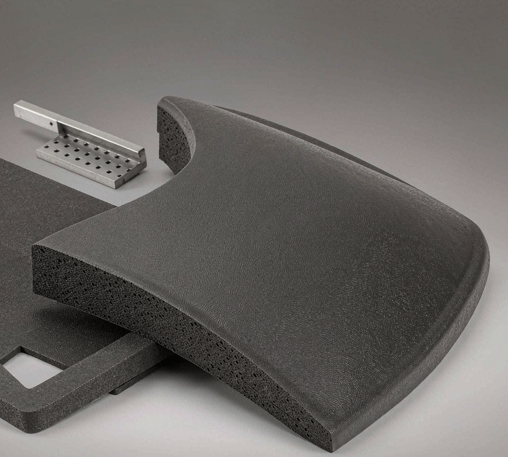 Cutaway of a molded charcoal EVA foam half-shell for a protective bag, with a die-cut EVA sheet and a small aluminum compression mold