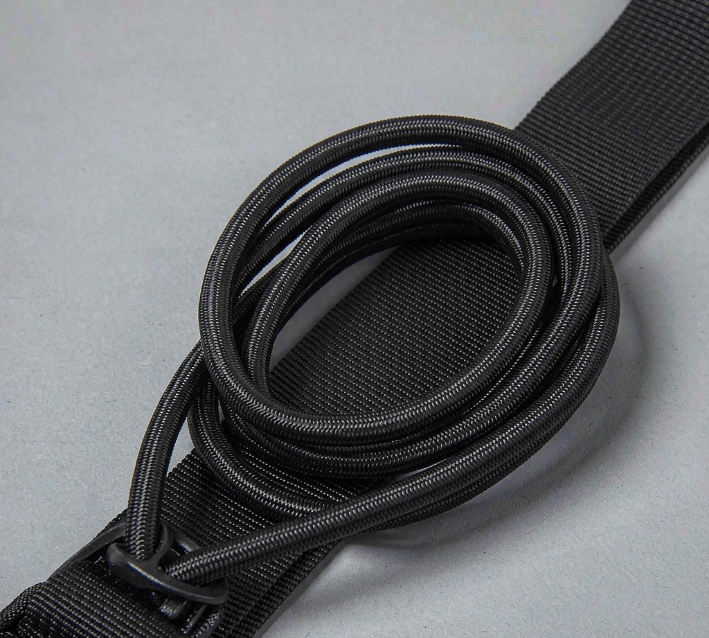 Coiled black shock cord with a woven polypropylene sheath, shown on a bag compression strap
