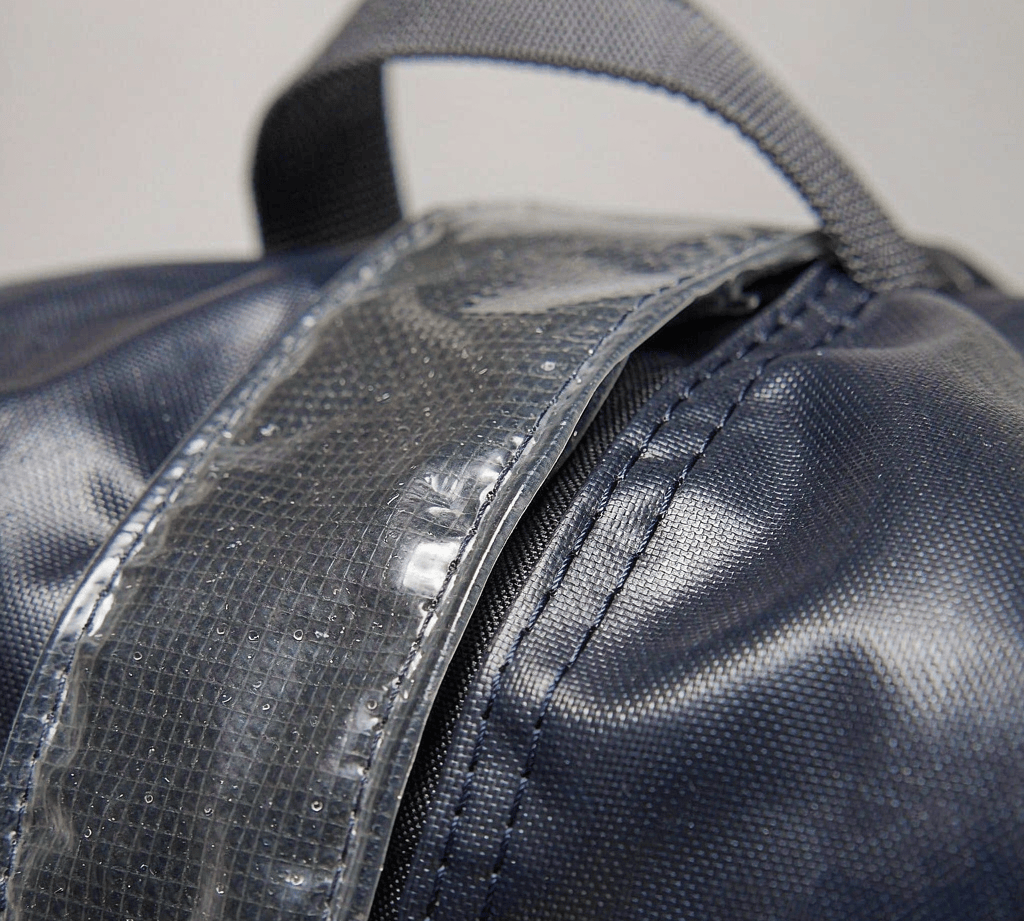 Close-up of a heat-taped waterproof backpack seam where glossy adhesive tape covers the stitching on a navy coated nylon panel