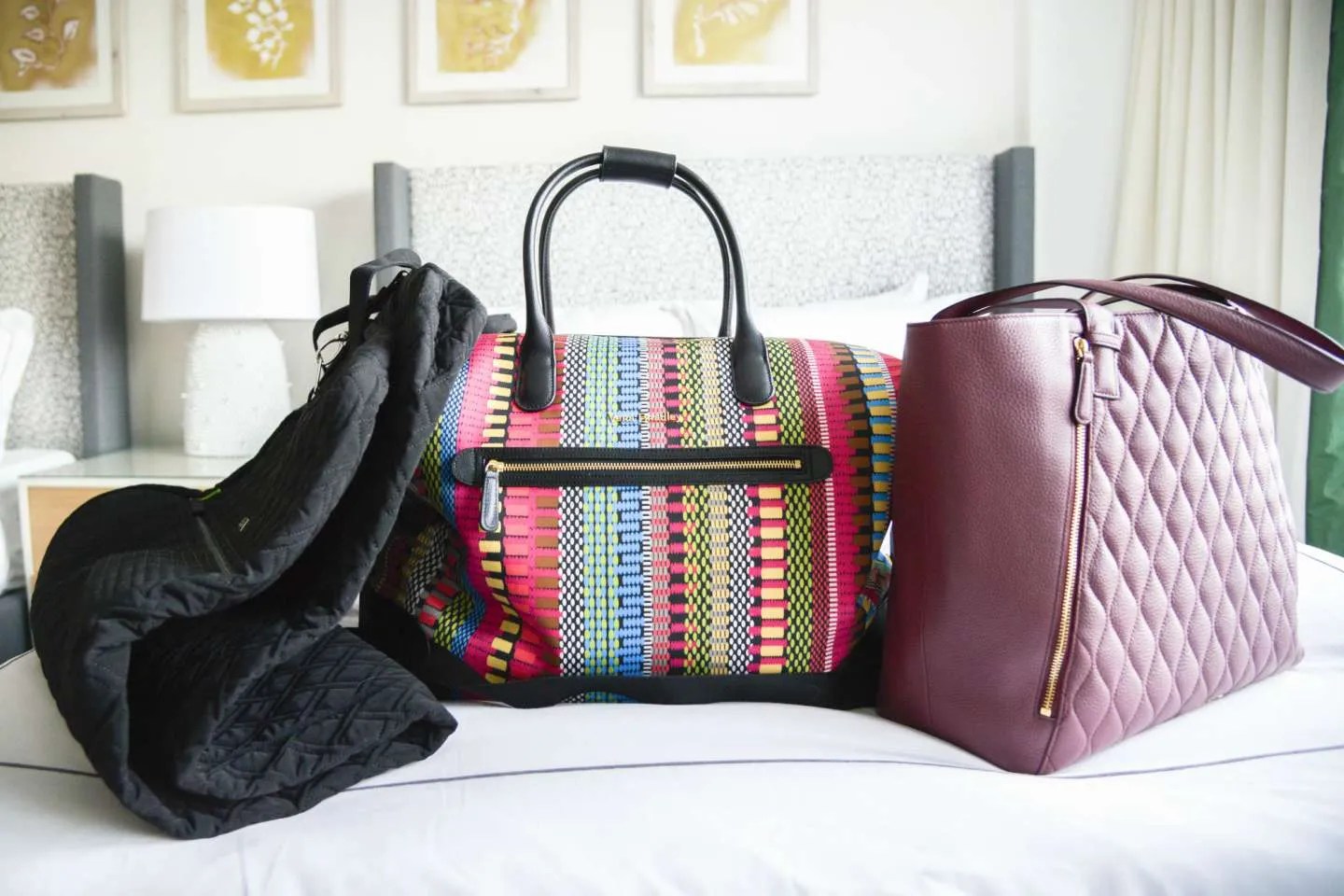 Three bags, including a garment bag, sit on a bed in a boutique hotel
