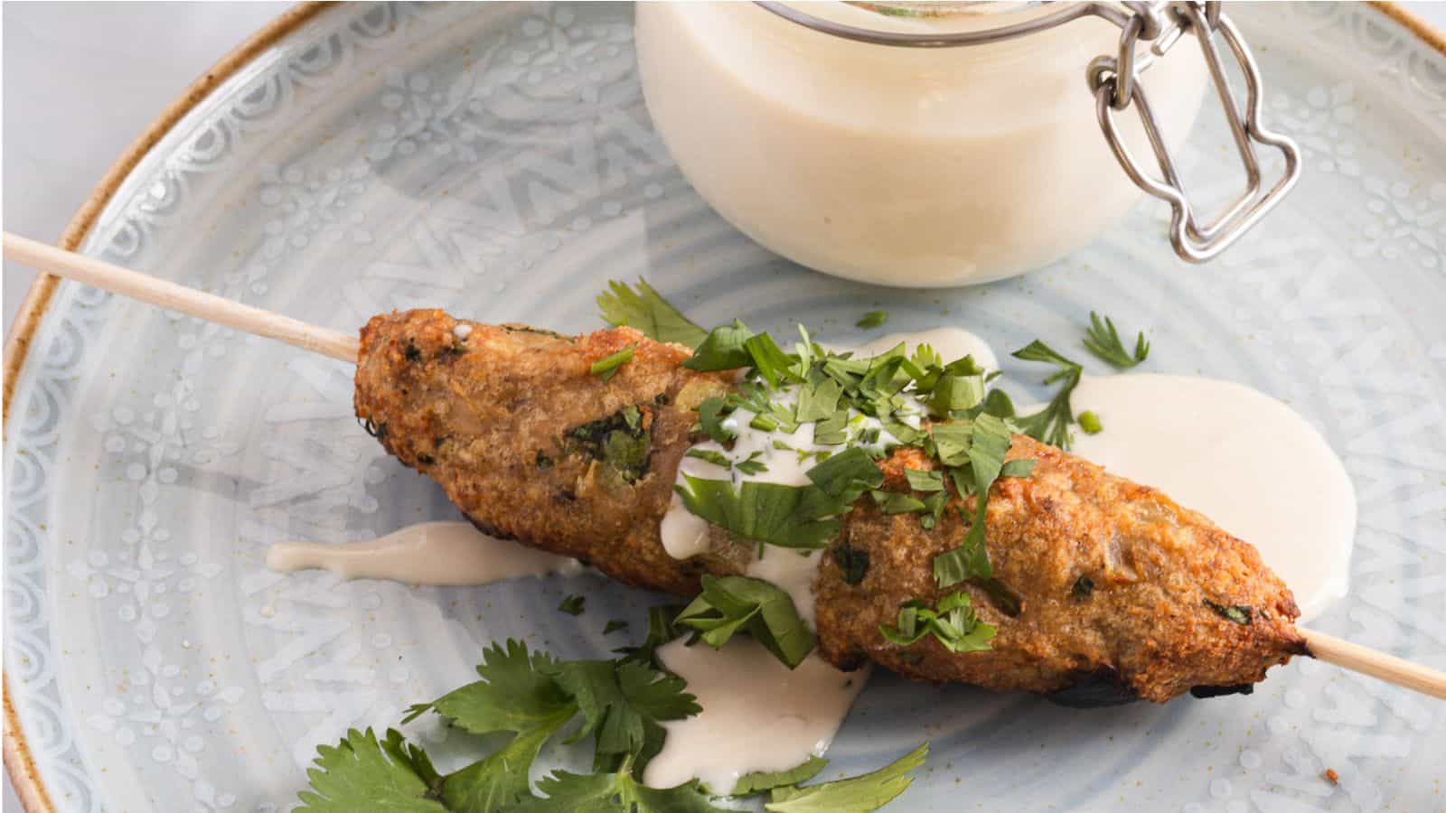Grilled Grandma's Chicken skewers garnished with fresh herbs and served with a side of creamy sauce on a decorative blue plate.
