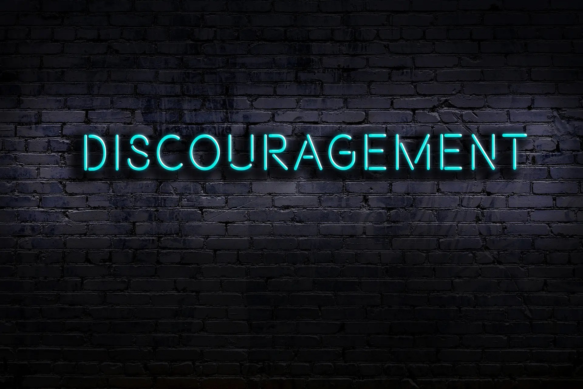 Photo of a darkened brick wall with Large subdued blue letters of the word DISCOURAGEMENT