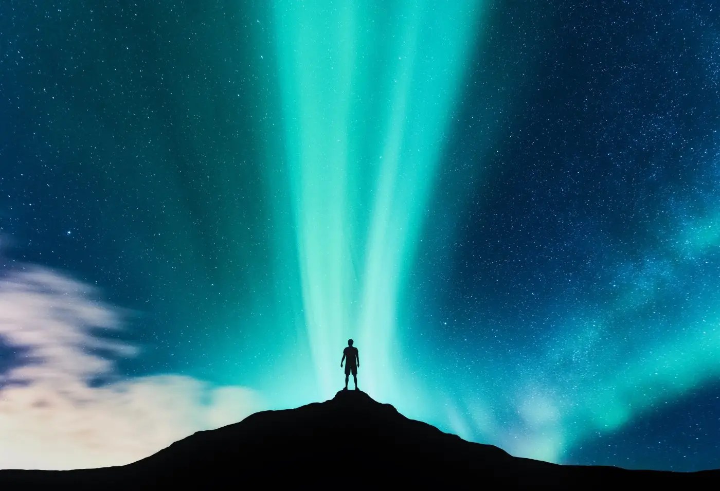 Aurora borealis and silhouette of standing man on the mountain. Starry sky and green polar lights. Night landscape with northern lights.