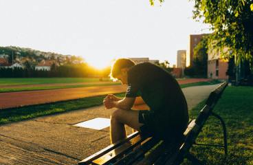 man sitting on bench near track field while sun is setting