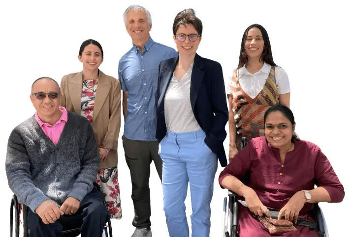 CIP staff members posing together outdoors, with two wheelchair users seated in front and four colleagues standing behind them.