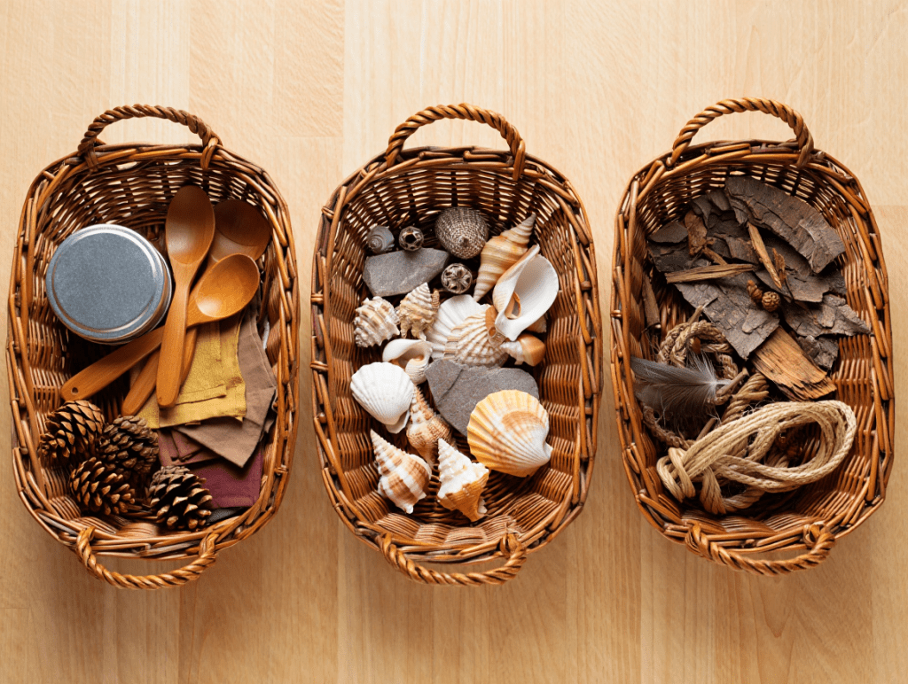 5 Sensory-Friendly Curiosity Approach Ideas for Special Needs Education 2 Three wicker baskets filled with various natural and everyday objects, including pinecones, wooden spoons, fabric swatches, seashells, and pieces of bark, arranged on a wooden surface.