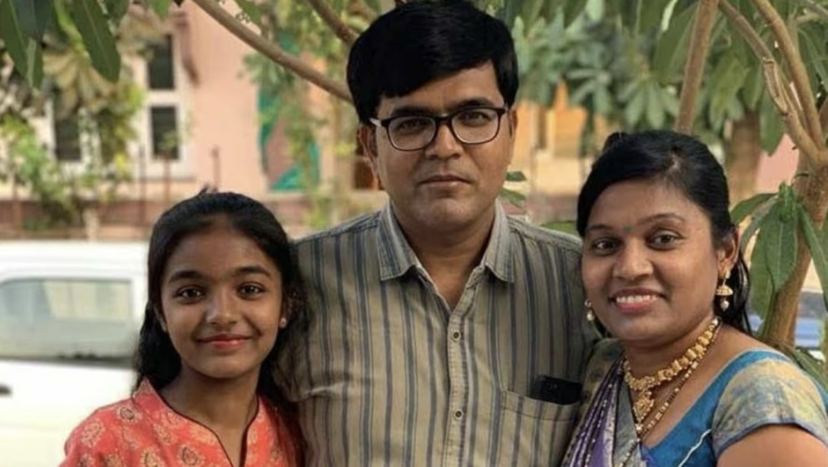 A family of a father with his arms around his wife and daughter