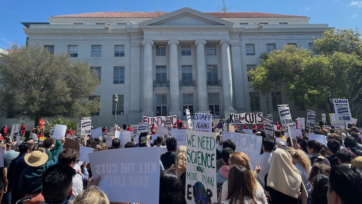 A crowd of protestors hold up signs on a university campus.