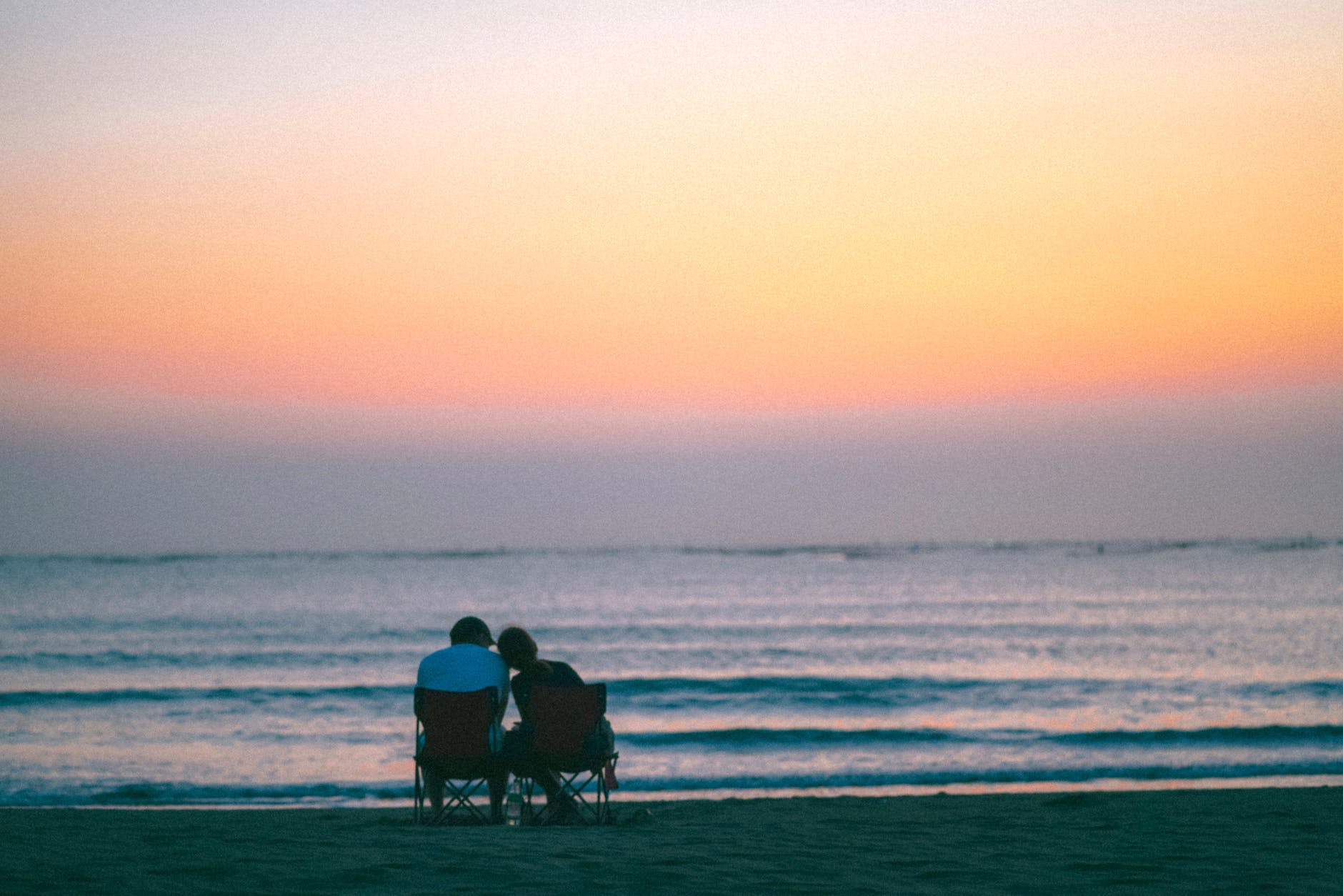 two people sitting on a beach at sunset