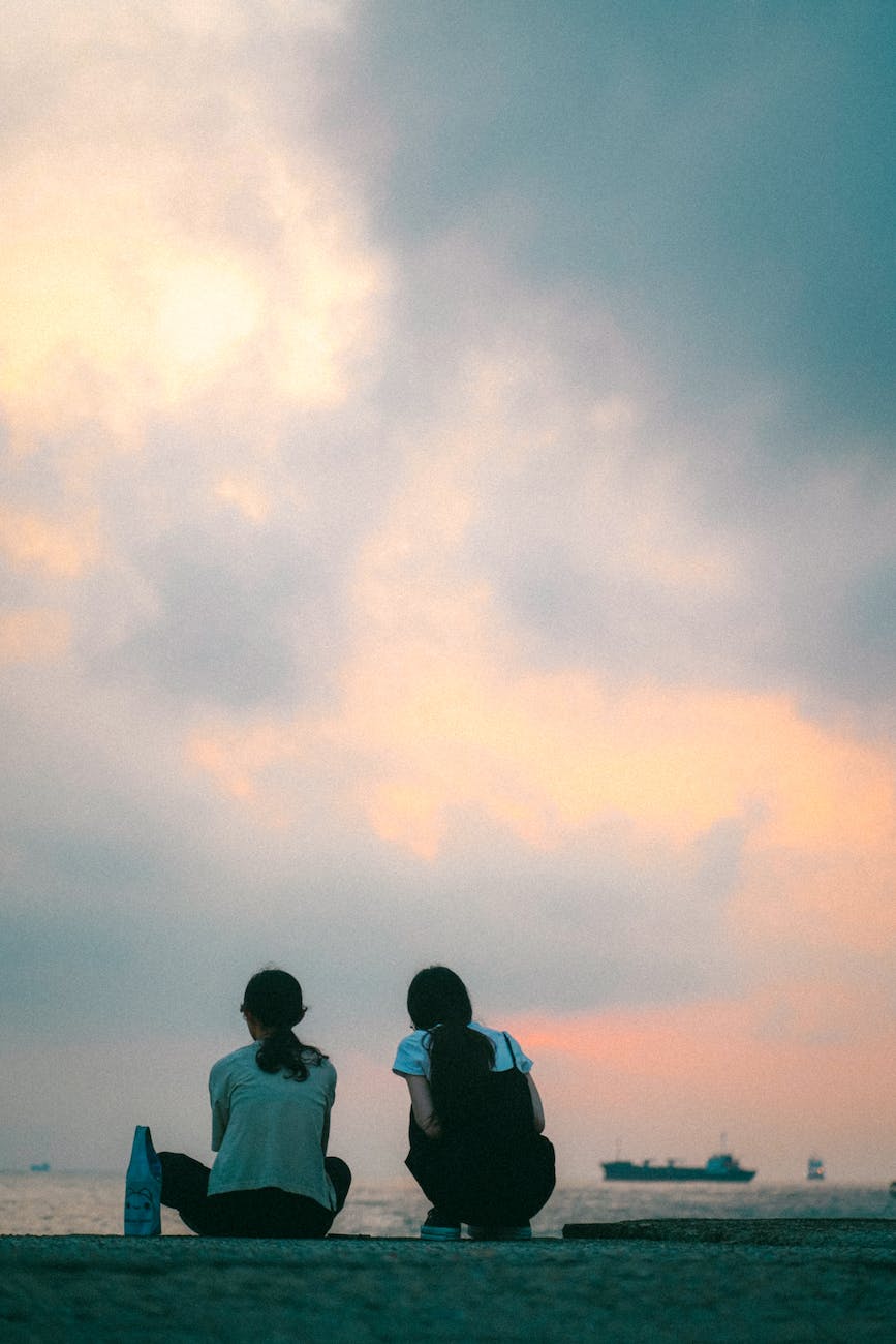 two people sitting on the beach at sunset