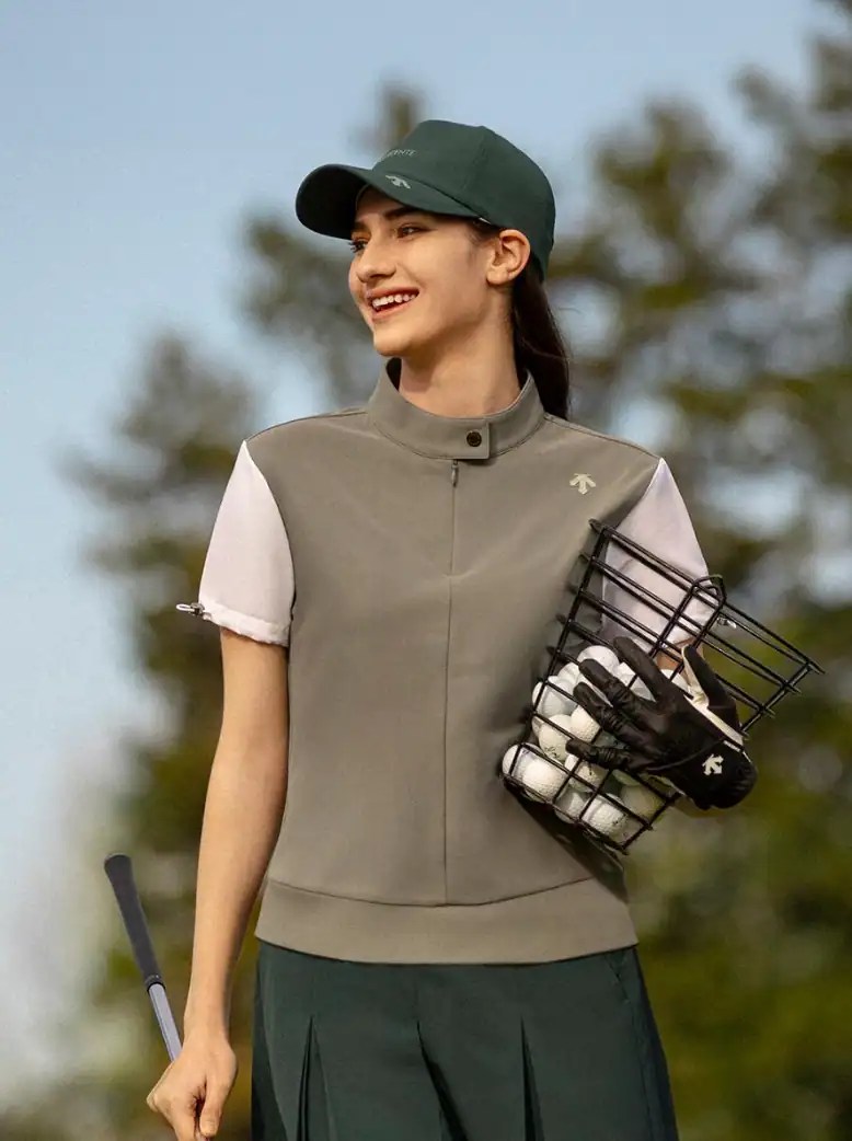 Golf woman smiling outdoors in sporty attire and cap, holding golf balls and club.