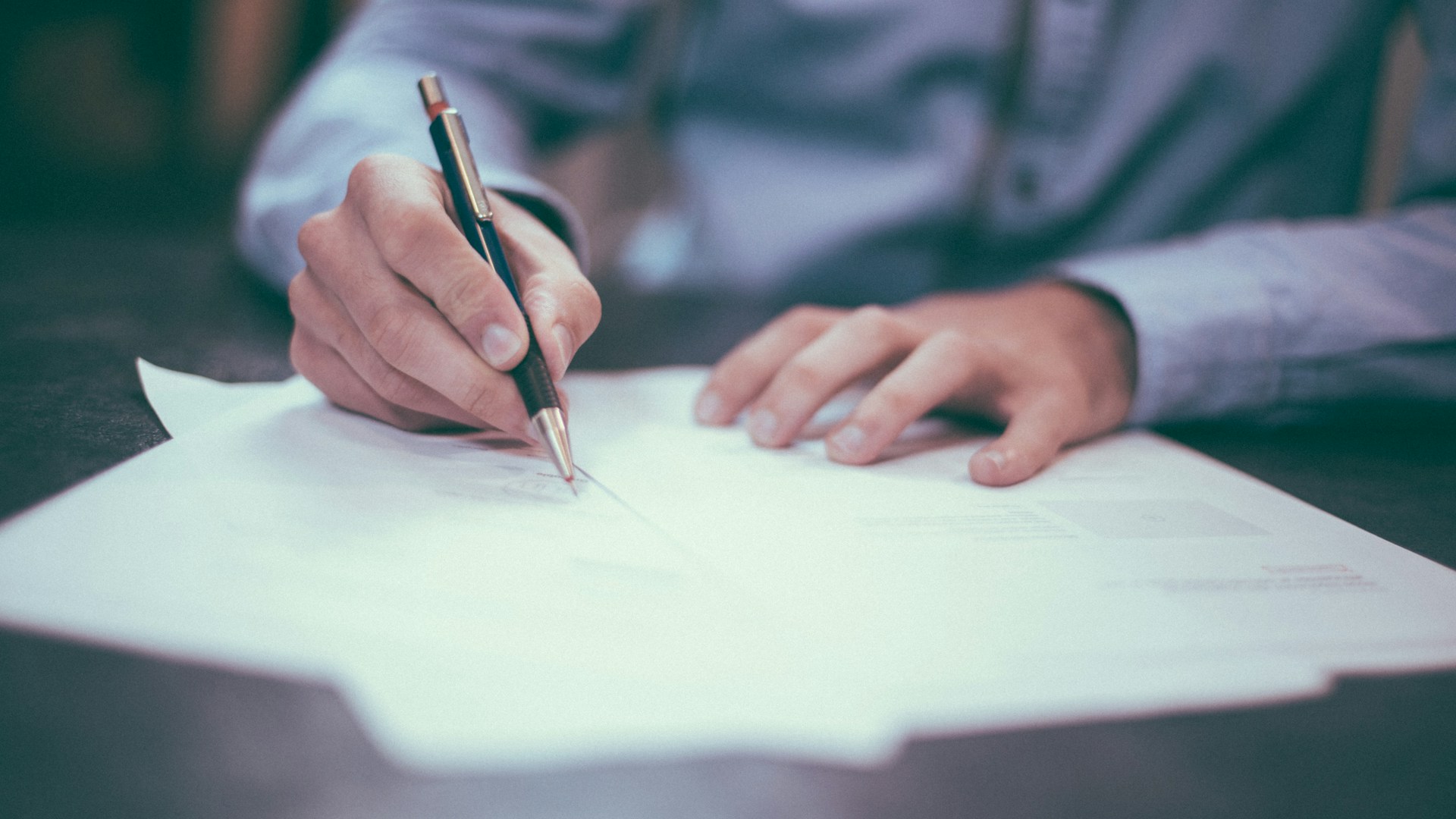Una persona firma un documento sobre una mesa de trabajo
