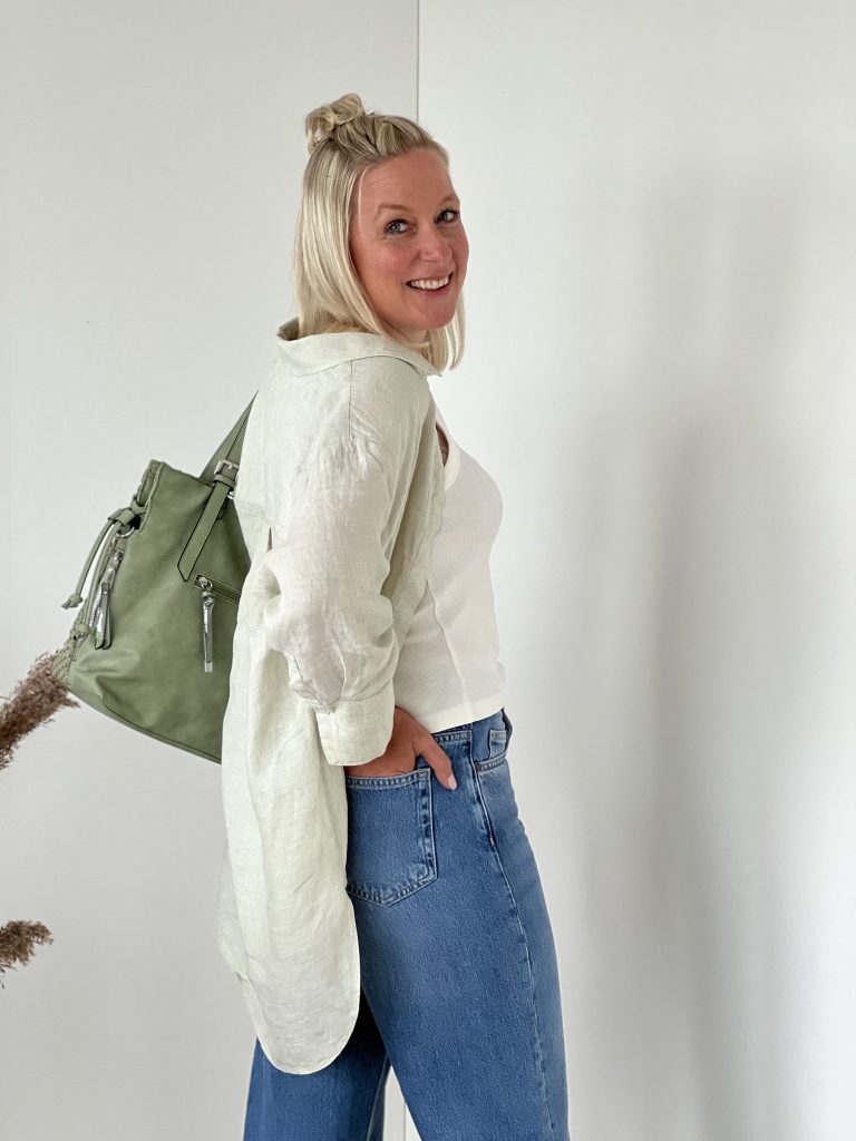 kühle Farben: Frau in blauer Jeans, hellem Oberteil und grüner Tasche über der Schulter