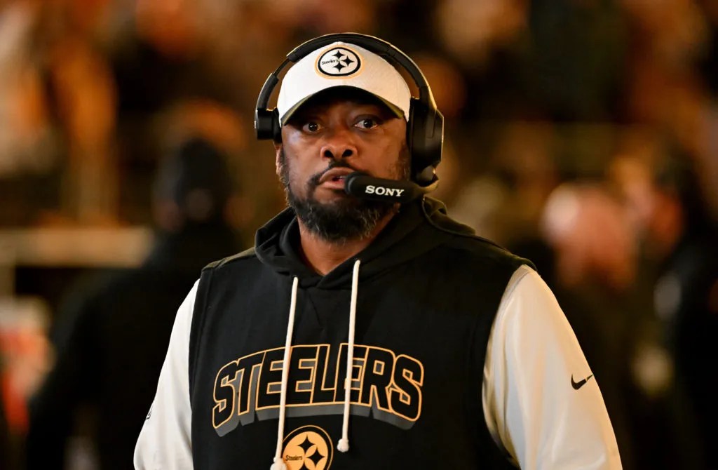 Tomlin standing on the sideline during an NFL game, wearing Steelers gear and looking focused.