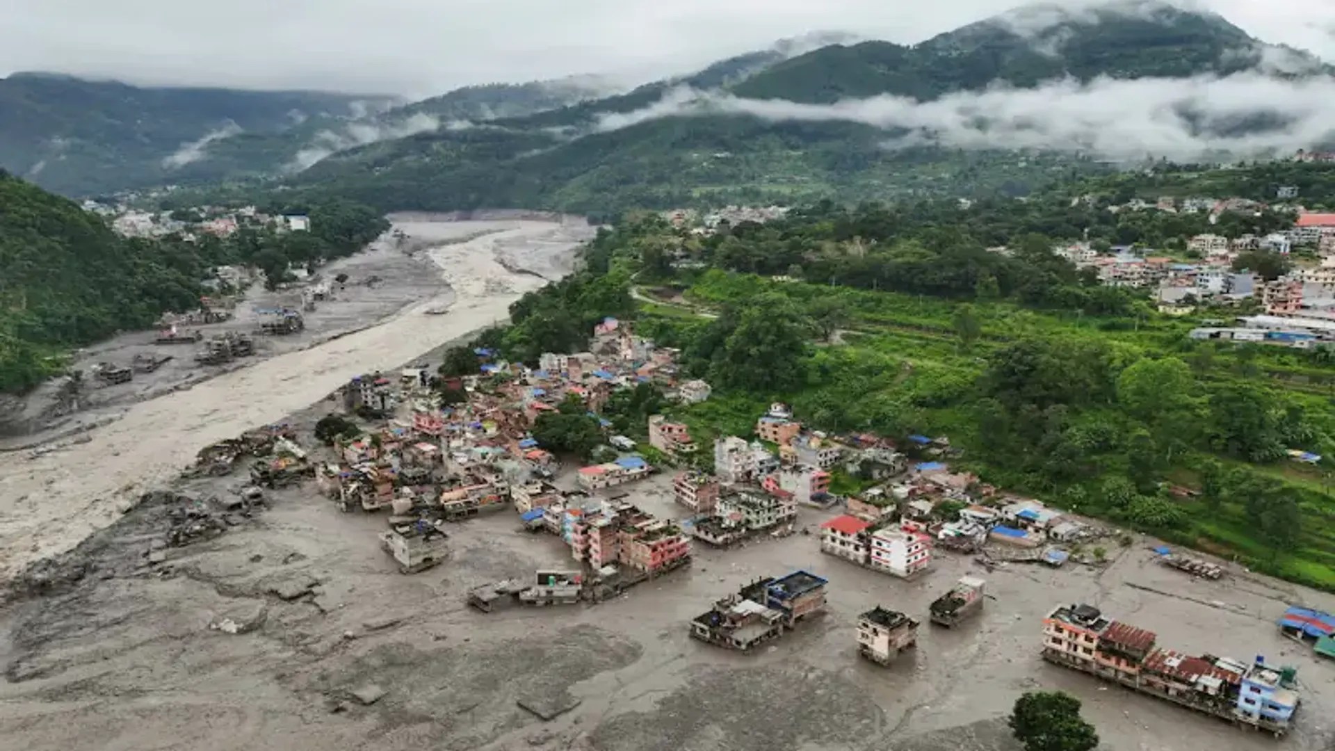 Aerial photograph of flood damage and mud along a river valley in Nepal; photograph published by Aaj English TV in August 2026.
