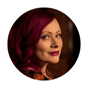 Profile photo of Heather Levy, the author of "Walking through Needles." She has magenta-colored hair and is looking over her shoulder with a subtle smile, set against a softly lit background.